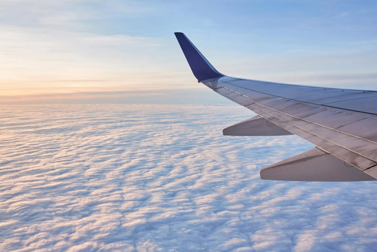 Aeroplane wing above the clouds, flight booking from Kampala
